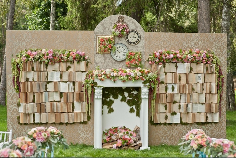 A whimsical wedding backdrop with vintage books, blooms, greenery, a fake fireplace and clocks is a beautiful idea for a vintage tea party wedding