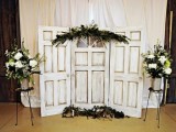 a vintage door and greenery wedding backdrop plus greenery and white florals on stands is a very cozy and cute idea