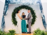 a round greenery wedding arch plus some tie dye blue fabric over will bring an outdoor feel indoors and will accent the couple