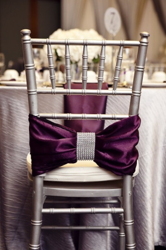 A silver chair with a deep purple bow and embellishments plus a purple napkin for an exquisite touch