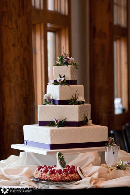 A white patterned wedding cake decorated with purple ribbons