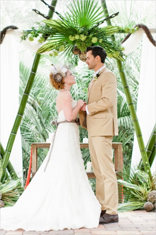 a safari tropical wedding arch of bamboo and with greenery and blooms is a bold and fun idea