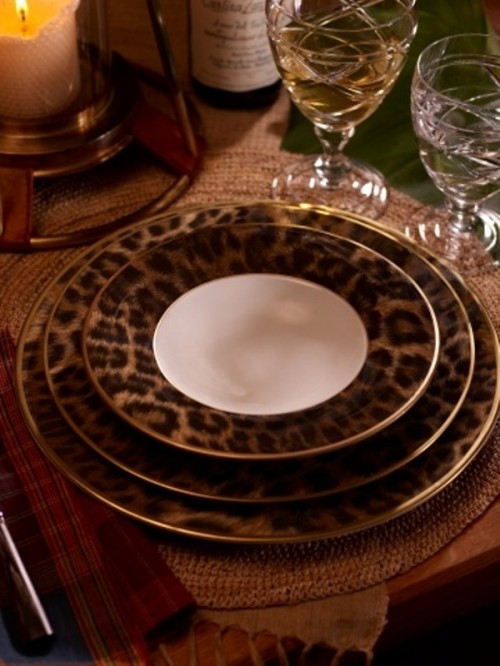 a safari wedding tablescape with leopard plates with a gold edge, candles, woven chargers and glasses