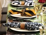 a bright safari-themed wedding table with tropical leaves, white plates and safari-themed napkins with embellished napkin rings and yellow glasses