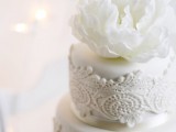 a white lace wedding cake topped with a large fresh white bloom is a beautiful and chic option for any wedding