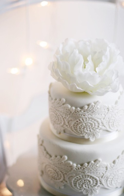 A white lace wedding cake topped with a large fresh white bloom is a beautiful and chic option for any wedding