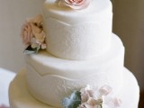 a white lace wedding cake decorated with sugar blooms in blush and white and greenery