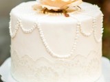 a white wedding cake decorated with sugar lace and pearls plus sugar blooms and leaves on top