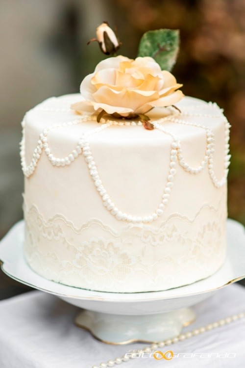 a white wedding cake decorated with sugar lace and pearls plus sugar blooms and leaves on top