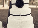 a white lace wedding cake decorated with ribbons and a black fabric flower for a monochromatic vintage wedding