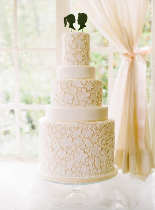 a tan wedding cake decorated with white edible lace and black head silhouettes as toppers for a catchy touch