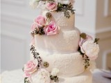 a white lace wedding cake topped with fresh pink and white blooms and greenery looks very catchy and very fresh