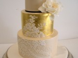 a tan and gold wedding cake decorated with white lace and a sugar bloom looks very glam-like