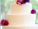 a white lace and tufted wedding cake decorated with purple and fuchsia fresh flowers