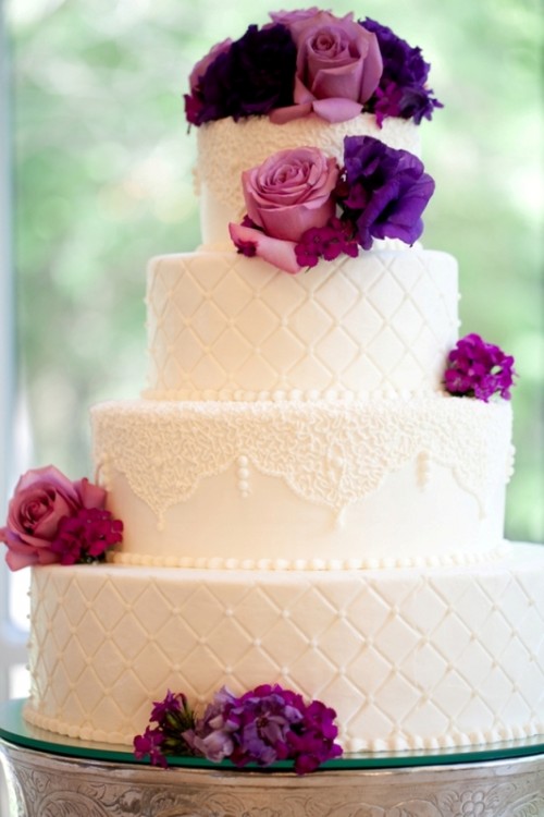 a white lace and tufted wedding cake decorated with purple and fuchsia fresh flowers