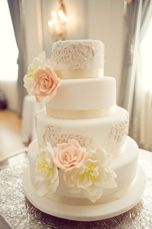 A white wedding cake decorated with tan lace and sugar blooms in pink and white is a cool idea to rock