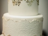 a beautiful white wedding cake decorated with white lace with a gold edge, gold decor on the upper tier
