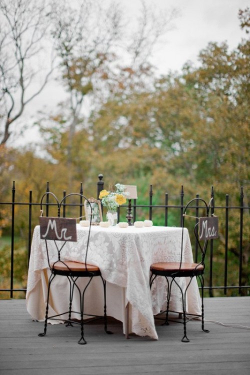 the sweetheart table accented with a white lace tablecloth, pumpkins, blooms and coordinating signage on the chairs