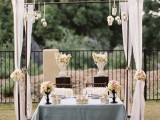 a sweetheart table decorated with lush white florals, candles and with a wedding arch with fabric, blooms and suspended candles
