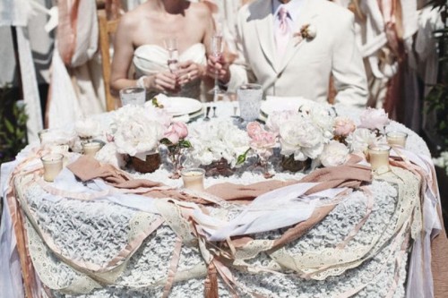a lace tablecloth, lots of ribbons that match in color and a table runner of white and pink blooms plus candles