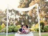 a lush and bright floral centerpiece and a wedding arch with fabric and suspended candles over the table