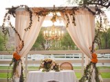 a sweetheart table accented with lots of blooms, a weddign arch with blush fabric and greenery plus a chandelier and some florals on the table