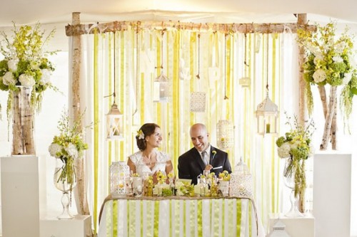 an arch with ribbons and candles and candle lanterns plus some cages, florals and branches around the sweetheart table
