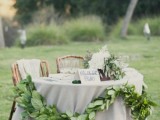 a greenery garland and a lush white blooms and greenery centerpiece to highlight the sweetheart table