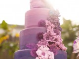 a bright wedding cake with an ombre effect, from light pink to lilac and purple, with lots of matching sugar blooms