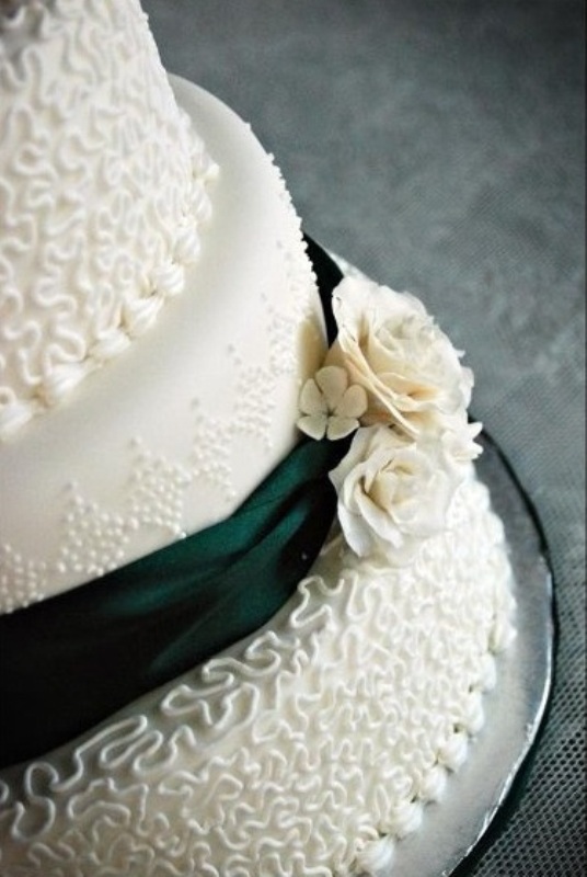 A textural white wedding cake decorated with green ribbons and sugar flowers
