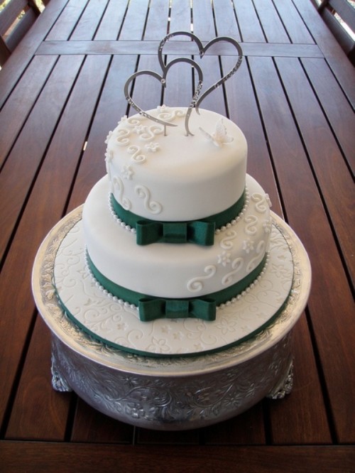 an elegant white wedding cake with patterns and emerald ribbons and bows
