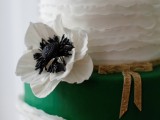 a white ruffle and sleek emerald wedding cake with gold touches and a sugar bloom