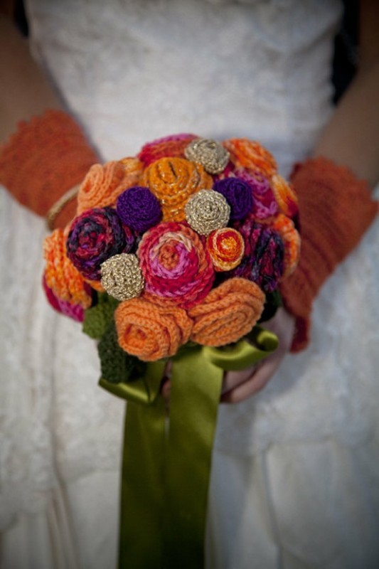 A colorful and bright knit flower wedding bouquet with green silk ribbons and matching mittens