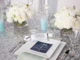 a silver glitter tablecloth paired with blue candles, white blooms and silver cutlery for a glam wedding reception