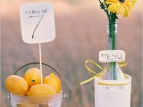 bold and simple spring wedding decor with a glass basket with lemons, a table number, a bottle with bold blooms