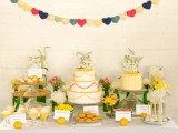 a bright and fun wedding dessert table with various sweets, bold blooms and greenery and a bold banner over it