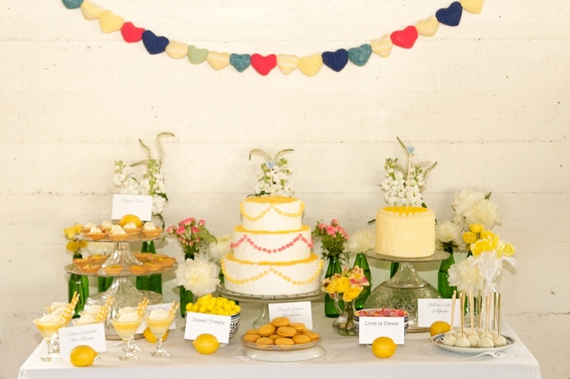 A bright and fun wedding dessert table with various sweets, bold blooms and greenery and a bold banner over it