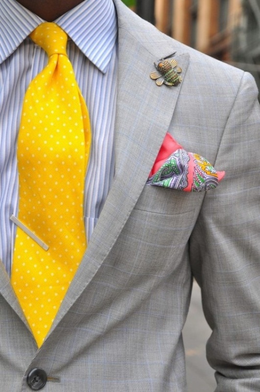 A bold and fun look with a grey plaid suit, a striped shirt and a yellow polka dot tie plus a colorful pocket square and a fun bee brooch