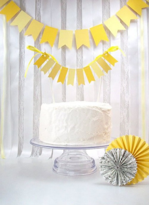 a white wedding cake with a bold yellow banner as a topper and a matching banner on the wall for a bright spring wedding