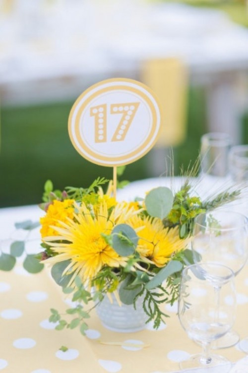 a bright wedding centerpiece with a bucket with greenery, bold yellow blooms and a printed table number