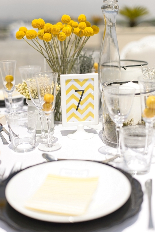 A bold wedding tablescape with billy balls, a bright table number and yellow menus, neutral linens and plates