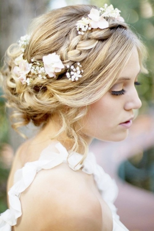 a messy updo with a braided halo plus pink roses and baby's breath for a romantic and relaxed bridal look