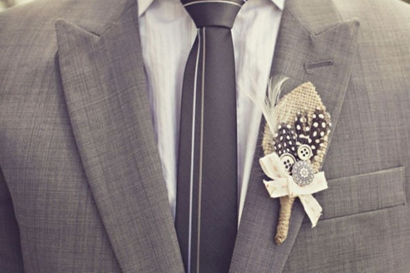 A grey suit, a white shirt, a grey striped tie and a cool feather boutonniere for a modern groom's outfit