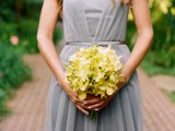 a grey sleeveless pleated maxi bridesmaid dress with a thin sash and a yellow bouquet to contrast it