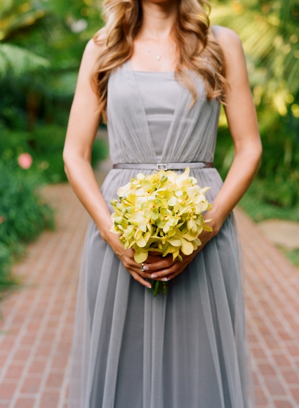 A grey sleeveless pleated maxi bridesmaid dress with a thin sash and a yellow bouquet to contrast it