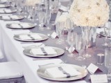 a silver grey table runner, matching plates, cards and candles paired with whites for a cool glam wedding tablescape