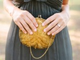 a grey one shoulder draped maxi bridesmaid dress with a gold beaded bag is a bold combo