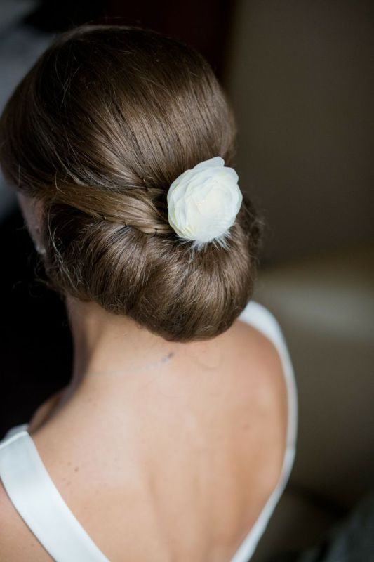 A modern twisted low updo with some sleek volume on top and a white faux bloom for a very refined and elegant look