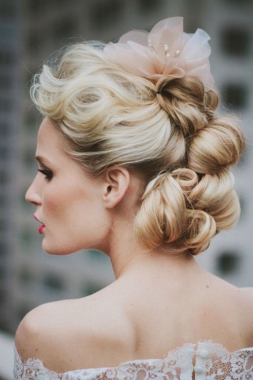 a messy and wavy low updo with a very quirky look and waves on top plus a blush fabric bloom with pearls for a unique looking bride