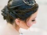 a twisted low updo with a braided halo and a small crown and some locks down is a stylish and chic idea with a modern feel